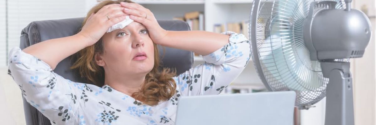 Woman dealing with air conditioner issues using a fan to stay cool.