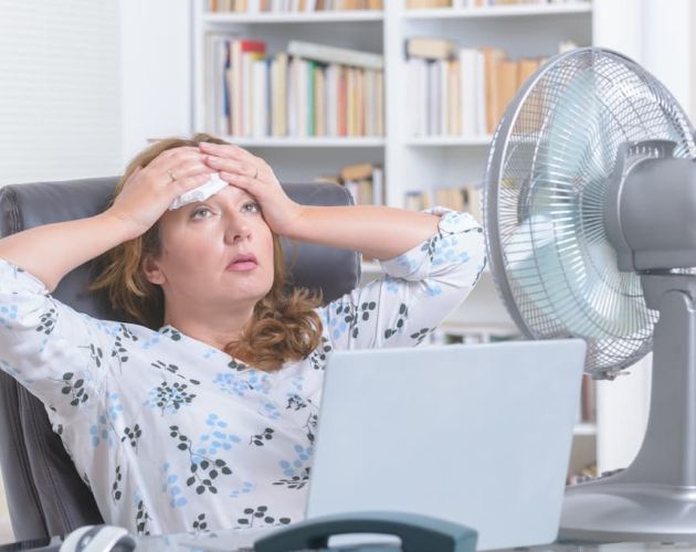 Woman dealing with air conditioner issues using a fan to stay cool.